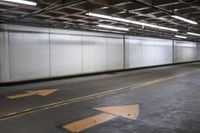 an empty concrete parking garage with no doors and a yellow arrow painted on the floor