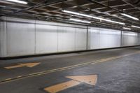 an empty concrete parking garage with no doors and a yellow arrow painted on the floor