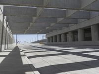 an open parking garage with concrete floors and long shadows on the floor and ceiling concrete structures in the area with large windows