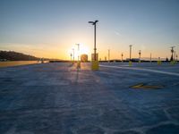 an empty parking lot is lit up at sunset with parking signs in the background and street lamps on either side