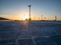 an empty parking lot is lit up at sunset with parking signs in the background and street lamps on either side