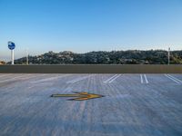 a parking lot with an arrow painted on the surface of it and signs in the background