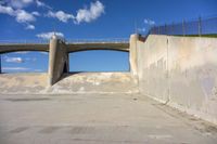 a bridge over a cement walkway in an empty parking lot with an old fashioned skateboard ramp