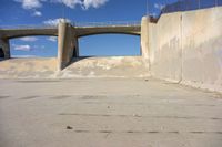 a bridge over a cement walkway in an empty parking lot with an old fashioned skateboard ramp