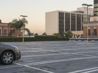 a car sits in a parking lot in front of a building and office buildings at dusk