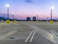 a parking lot is lit up at night with a city skyline in the distance by several tall street lamps