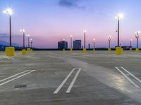 a parking lot is lit up at night with a city skyline in the distance by several tall street lamps