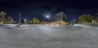 an empty parking lot with a lit up building and lamp posts in the middle of the road