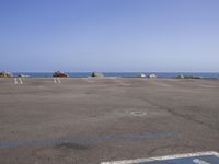 an empty parking lot near the water with rocky shoreline in the background during the day