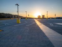 a paved parking lot with several poles and lights, on sunset time, with the sun rising