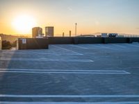 the sun is setting on a building with parking lot with white lines in it and buildings in the background