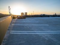 the sun is setting on a building with parking lot with white lines in it and buildings in the background