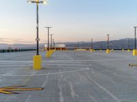 an empty parking lot in front of multiple lights with mountains in the distance during sunset