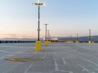 an empty parking lot in front of multiple lights with mountains in the distance during sunset