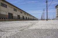 a long paved concrete road with large industrial buildings next to it and overhead electrical wires