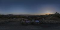 a bench overlooking a landscape of houses on a hill at dusk with the sun shining