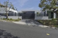 a street with trees, shrubs and bushes in front of a gray building with a gate