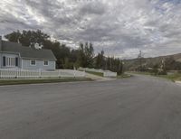 a street view of a residential area with a white picket fence on both sides and hills in the background