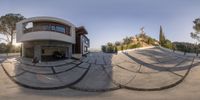 a 360 - angle photograph of an outdoor living space with a curved concrete building near a hillside in the background