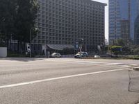 some cars on the road near buildings and trees in a large city street area with tall buildings