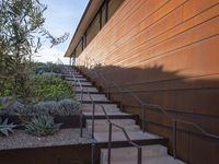 a set of stairs is next to an orange building and a tree and some bushes