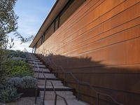 a set of stairs is next to an orange building and a tree and some bushes