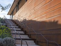 a set of stairs is next to an orange building and a tree and some bushes