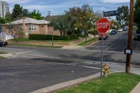 a stop sign is by some grass and buildings in a neighborhood in the sunshine, on a residential road