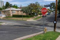 a stop sign is by some grass and buildings in a neighborhood in the sunshine, on a residential road