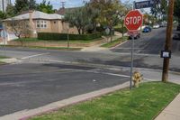 a stop sign is by some grass and buildings in a neighborhood in the sunshine, on a residential road