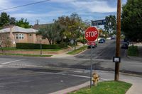 a stop sign is by some grass and buildings in a neighborhood in the sunshine, on a residential road