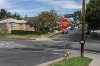 a stop sign is by some grass and buildings in a neighborhood in the sunshine, on a residential road