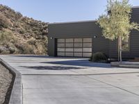 a cement driveway with cement steps and concrete driveway in the foreground to a hillside house with grey sidings