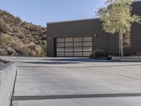 a cement driveway with cement steps and concrete driveway in the foreground to a hillside house with grey sidings