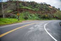 a curve in a country road with yellow lines going through the mountainside on the right