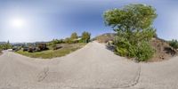 a panoramic view of a street with parked cars in the driveway and houses on the hill