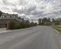 a quiet residential street is lined with homes and trees in the background the cloudy sky has a light blue and gray color