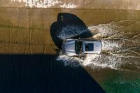 a vehicle drives through a body of water and in the sun, above the sidewalk