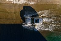 a vehicle drives through a body of water and in the sun, above the sidewalk