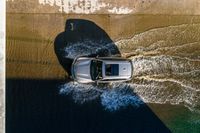 a vehicle drives through a body of water and in the sun, above the sidewalk