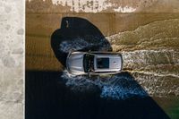 a vehicle drives through a body of water and in the sun, above the sidewalk