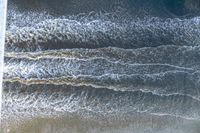 an overhead image of an ocean scene with surfers, and waves crashing towards the shore