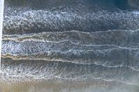 an overhead image of an ocean scene with surfers, and waves crashing towards the shore