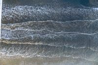 an overhead image of an ocean scene with surfers, and waves crashing towards the shore