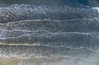 an overhead image of an ocean scene with surfers, and waves crashing towards the shore