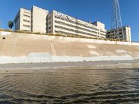 a river that is running on sand near a bridge with power lines and apartment buildings behind it