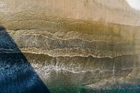 an aerial view of waves coming into the shore and a person standing on a surfboard