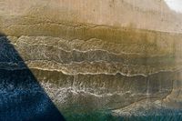 an aerial view of waves coming into the shore and a person standing on a surfboard