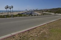 a street and beach line with palm trees at the edge of the road and cars
