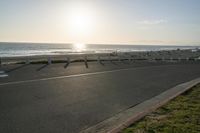 an empty road near a beach and waves as well as cars on the sand and houses on the beach